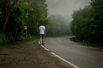 A man is hitchhiking near the mountain road