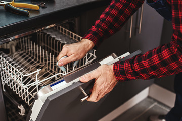 Repairing dishwasher. Close-up of man technician sitting near dishwasher