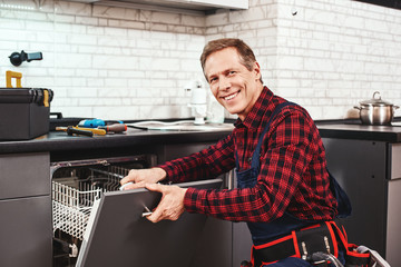 Call the professional. Male technician sitting near dishwasher and smiling