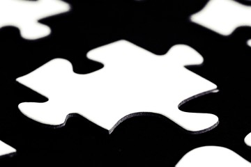 White puzzle pieces against a black background with a certain distance between the individual parts - concept for sub-steps or sub-elements of a large whole presented with puzzle pieces