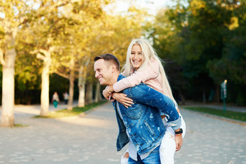 Happy couple on vacation. Lovers are laughing. Happy guy and girl. Lovers enjoy each other in the sunny park. Boyfriend carrying his girlfriend on piggyback