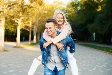 Happy couple on vacation. Lovers are laughing. Happy guy and girl. Lovers enjoy each other in the sunny park. Boyfriend carrying his girlfriend on piggyback