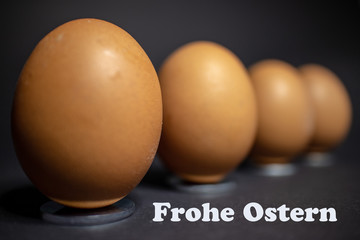 Anordnung von mehreren Eiern für Ostern vor schwarzen Hintergrund.Mit dem Text Frohe Ostern in deutscher Sprache.