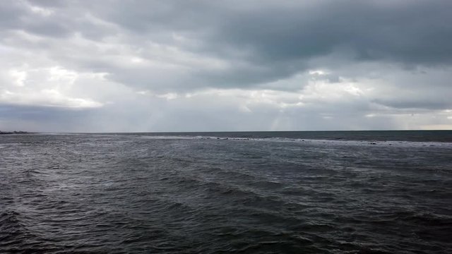 Dramatic weather over the sea threatening waves crashing at the shore with overcast sky and sunbeams on the water