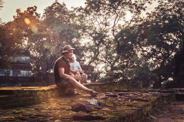 Man traveler with child daughter resting together on ruins at sunset during vacation concept travelling lifestyle  