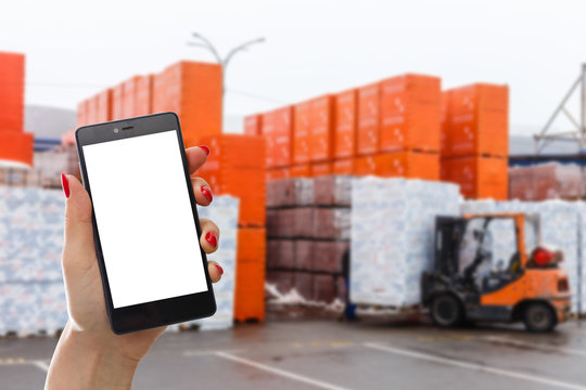 Hand holding smartphone against warehouse worker loading up pallet - Powered by Adobe