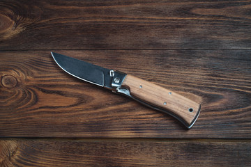 hunting bowie knife with a wooden handle on dark wooden background. Steel arms weapon. top view - obrazy, fototapety, plakaty