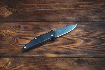 hunting bowie knife with a black plastic handle on dark wooden background. Steel arms weapon. top view