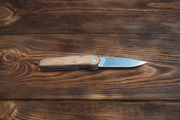 hunting bowie knife with a wooden handle on dark wooden background. Steel arms weapon. top view