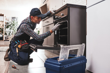 Don't delay with repair. Close-up of repairman examining oven - obrazy, fototapety, plakaty