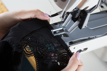 sewing process on sewing professional manufacturing machine with metal needle detailed by white caucasian woman's hands holding lace fabric for lingerie production