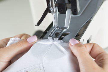 sewing process on sewing professional manufacturing machine with metal needle detailed by white caucasian woman's hands holding lace fabric for lingerie production