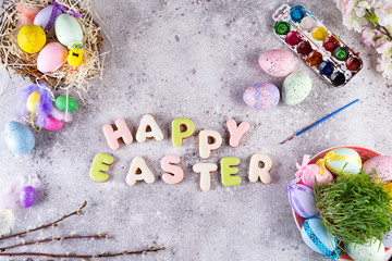 Easter eggs in a nest of grass, homemade glazed cookies and paints for painting eggs and grass as attributes of the preparation of the Easter holiday on a stone background, flat lay