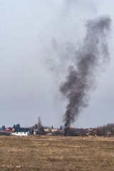 Fototapeta na wymiar Black Smoke Rising to the Sky from a Field on a Sunny Winter Day