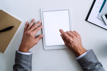 A midsection of businessman sitting at the table, using tablet. A top view. Copy space.