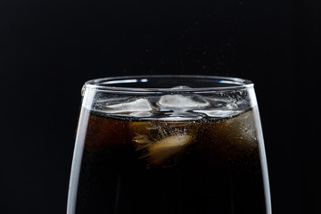Glass of pouring fizzy drink with ice on a black background