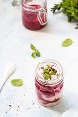 Tasty cottage cheese parfait with raspberry sauce and mint in a glass jar. Diet dessert. Light grey stone concrete background. Copy space.