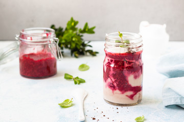 Tasty cottage cheese parfait with raspberry sauce and mint in a glass jar. Diet dessert. Light grey stone concrete background. Copy space.