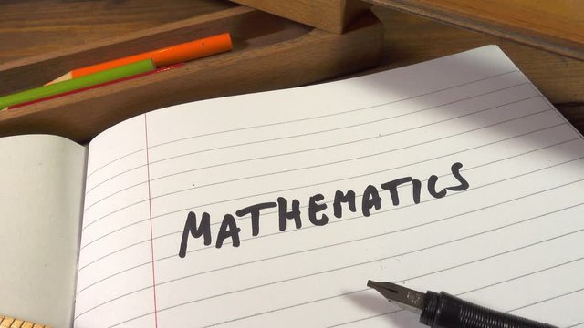 Track up over an exercise book marked mathematics with a wooden ruler pen and wooden pencil case on an old wooden school desk.