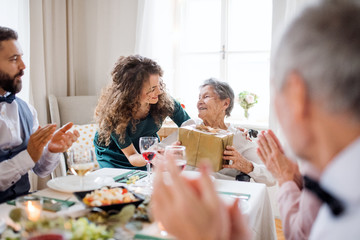 An elderly grandmother celebrating birthday with family and recieving a gift, party concept.