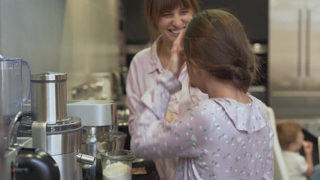 The mother and the daughter have some fun while cooking. They takys little amount of flour and put on daughter's face in order to make funny faces. Girl turns around to camera every couple of seconds.