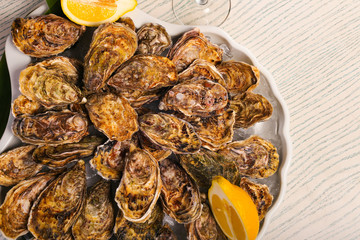 big plate of oysters with two lemons and vine on black wood background 