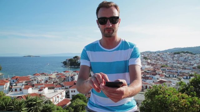 Man using cellphone with Skiathos, Greece panorama in the background.
