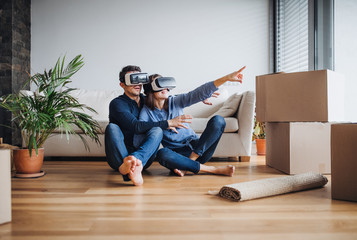 A young couple with VR goggles sitting on a floor, moving in a new home.