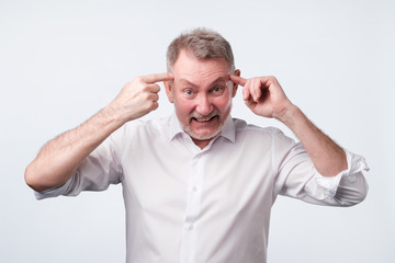 Angry senior man gesturing with his finger against temple asking are you crazy