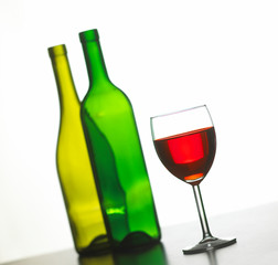 GLASS OF RED WINE WITH TWO GREEN WINE BOTTLES ON WHITE BACKGROUND