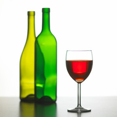 GLASS OF RED WINE WITH TWO GREEN WINE BOTTLES ON WHITE BACKGROUND