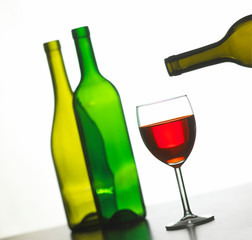 GLASS OF RED WINE WITH TWO GREEN WINE BOTTLES ON WHITE BACKGROUND