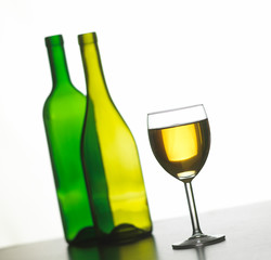 GLASS OF WHITE WINE WITH TWO GREEN WINE BOTTLES ON WHITE BACKGROUND