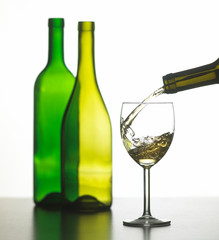 GLASS OF WHITE WINE WITH TWO GREEN WINE BOTTLES ON WHITE BACKGROUND