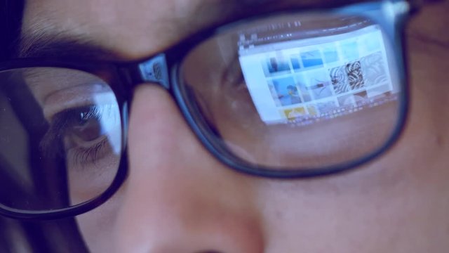 Close up footage of female with glasses looking at computer. Reflection of computer screen on woman glasses.