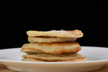 A stack of oatmeal pancakes in a white plate over a wooden background, opposite a black background