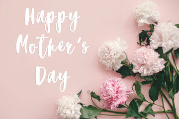 Happy Mother's Day text sign on peonies flat lay. Pink and white peonies border on pastel pink paper with space for text.  Stylish floral greeting card.