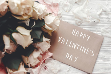 Happy Valentine's Day text sign on craft greeting card and  white roses bouquet on wooden background.  Valentines day floral greeting card..