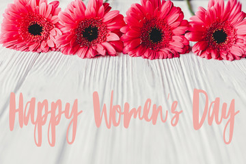 Happy Women's Day text sign at pink gerbera on white wooden background. Floral greeting card. Girl Power. International womens day, 8 march.