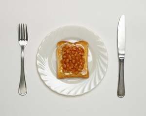 BAKED BEANS ON TOAST ON WHITE PLATE WITH KNIFE AND FORK
