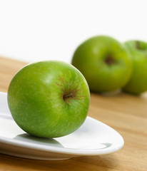 FRESH GREEN APPLE ON WHITE PLATE WITH GREEN APPLES IN BACKGROUND