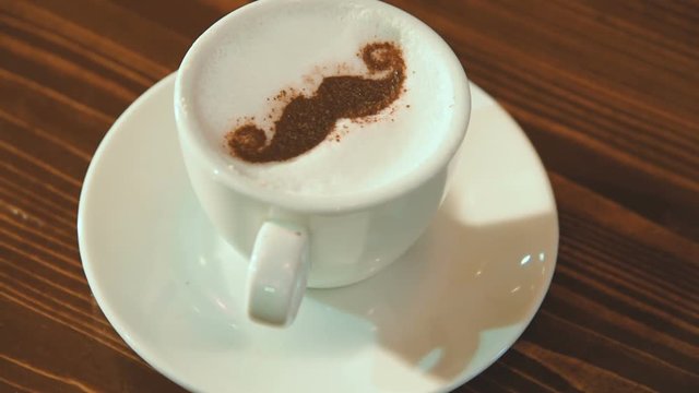 drawing on the foam of coffee or latte art in the form of a mustache close - up in the barbershop