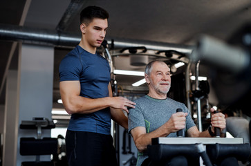 A senior man with a young trainer doing strength workout exercise in gym.
