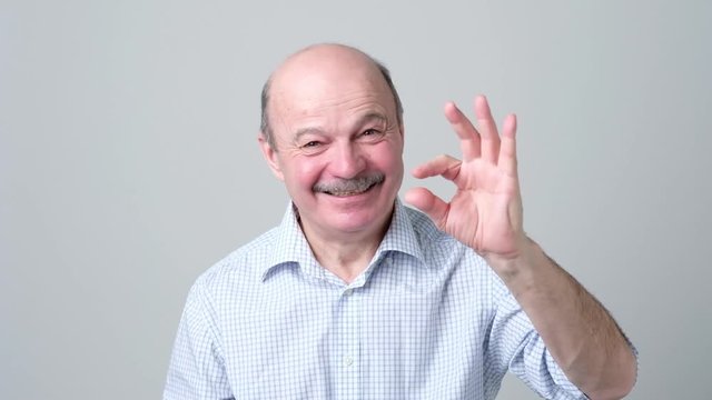 Senior man with mustache showing something small with figers.