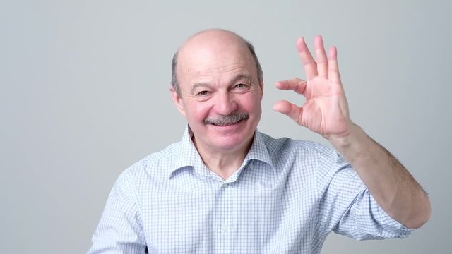 Senior man with mustache showing something small with figers.