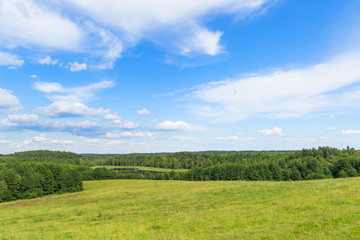 Fototapeta na wymiar Landscape of European plains with hills and lowlands, marshes, meadows and forests. Blue sky with clouds over horizon.