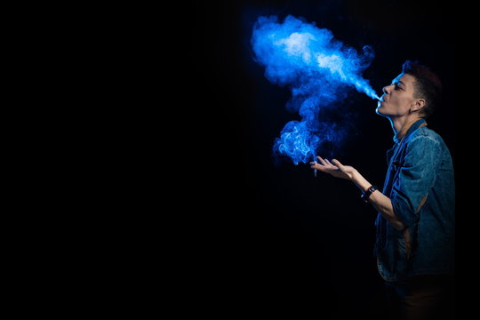 A woman with red hair in a denim suit smokes a cigarette and releases a bym in blue light on a black background