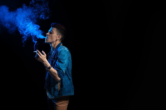 A woman with red hair in a denim suit smokes a cigarette and releases a bym in blue light on a black background
