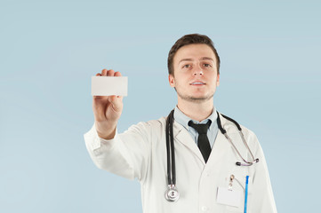 Doctor holding copy space. Close-up of a confident young doctor showing his business card and smiling while standing against blue background