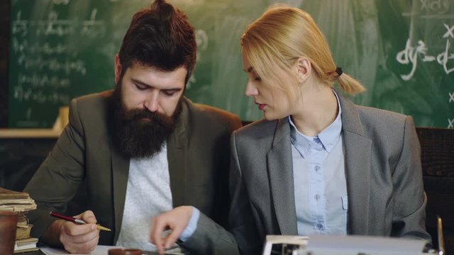 Teachers work at the table against the backdrop of a green board. Teachers work in classroom. Mathematical Formula Equation on the Blackboard. Teacher in classroom. Woman prints on a typewriter.